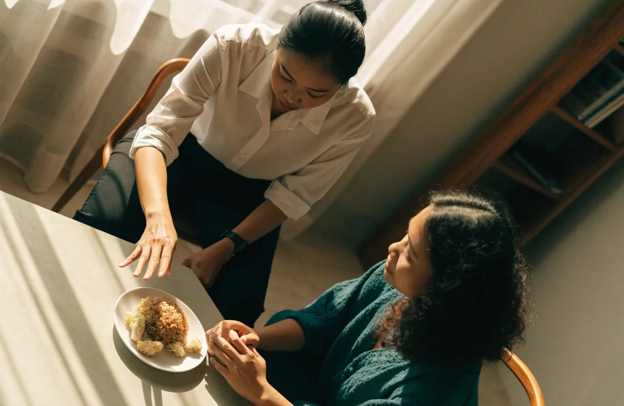 Two people seated across a light table during an online nutrition consultation, seen from above